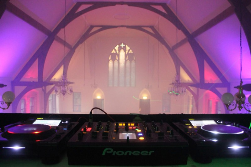DJ booth in a converted church venue washed in pink and purple uplighting