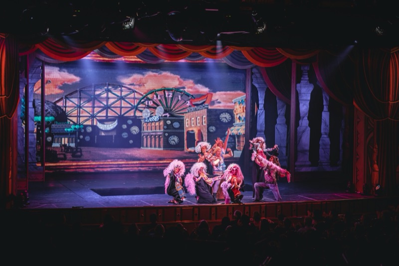 Musical theatre cast performing in front of a painted backdrop